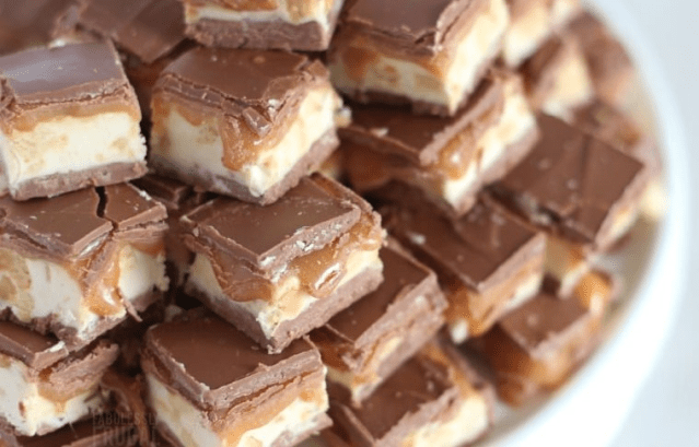 Multiple snickers fudge cut into squares all stacked on a plate.
